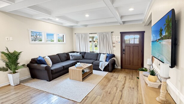 A modern living room with a sectional sofa, wooden coffee table, and a large flat-screen TV mounted on the wall.