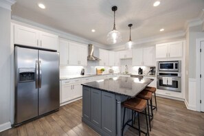 A modern kitchen with white cabinets, stainless steel appliances, a large island with bar stools, and pendant lighting. - Two Luxury Townhomes- Walk to Gulch - Skyline View (Nashville)