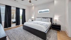 A modern bedroom with a large bed, a ceiling fan, and a window with a city view.