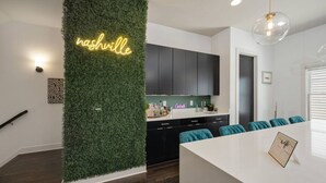 A modern kitchen with dark cabinets, a neon sign, and teal cushions on the dining table.