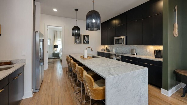 A modern kitchen with a marble island, dark cabinetry, and pendant lighting.