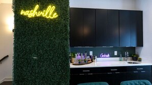 A modern kitchen with a neon sign reading "nashville," a bar area with a neon sign, and a green wall.