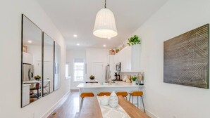 A modern kitchen with white cabinets, a wooden dining table, and a hanging pendant light.