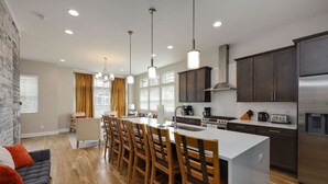 A modern kitchen with a central island, dark wooden cabinets, stainless steel appliances, and a large window providing natural light. - Two Townhomes - Hot Tubs and Rooftop Balconies (Nashville)