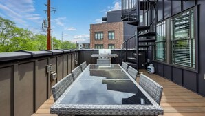 A rooftop deck with a glass-top table, wicker chairs, a grill, and a water feature. - Two Townhomes - Hot Tubs and Rooftop Balconies (Nashville)