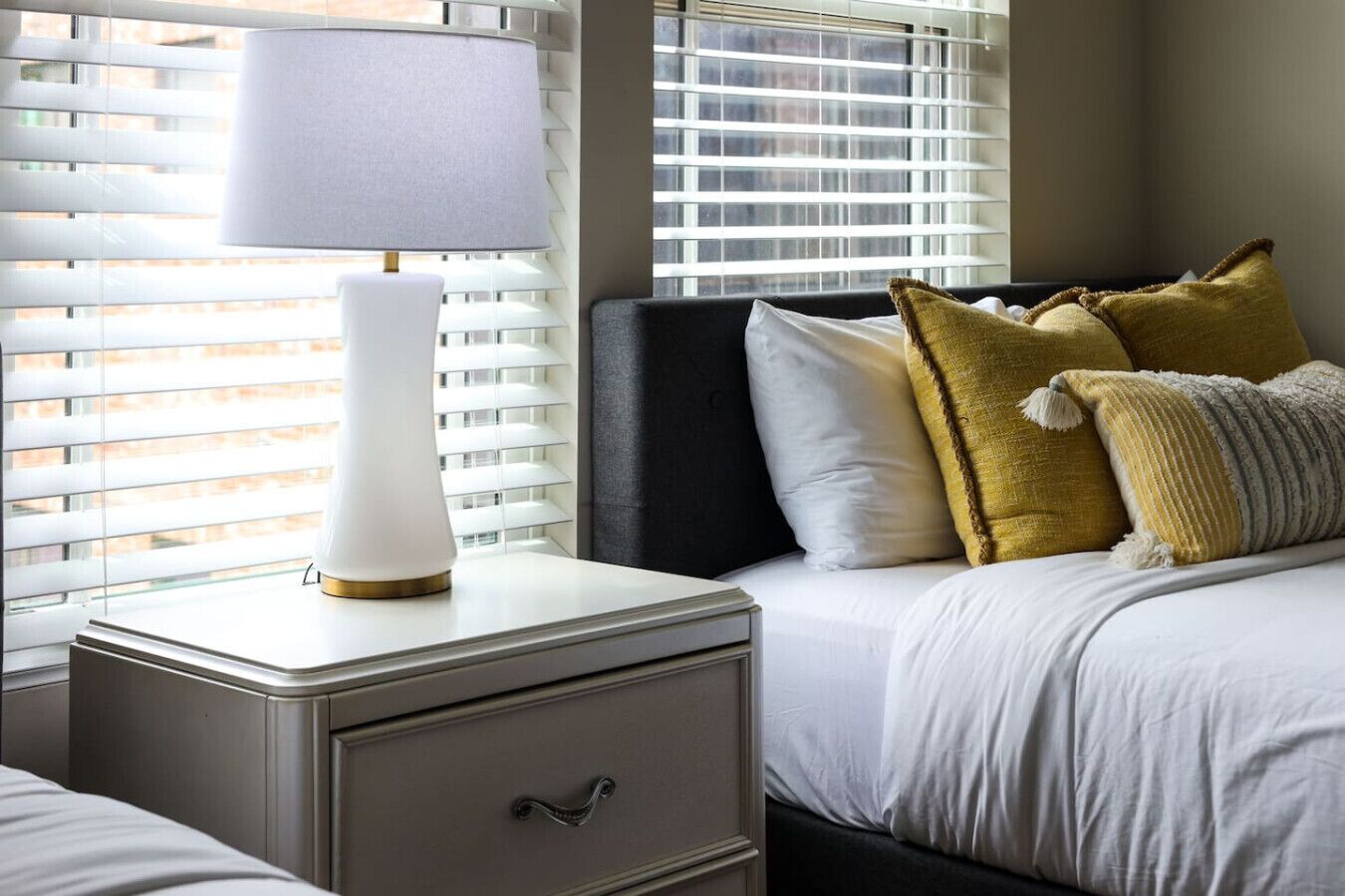 A neatly made bed with white bedding, a bedside lamp, and decorative pillows.