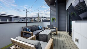 A modern outdoor seating area with a sofa, chairs, and a table, featuring a wooden deck and string lights.