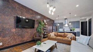 A modern living room with a large flat-screen TV, a brown leather sofa, a white couch, and a coffee table.