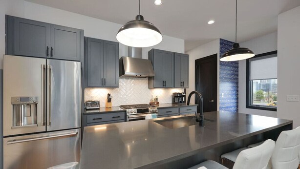 A modern kitchen with stainless steel appliances, grey cabinets, and a large island with bar seating.