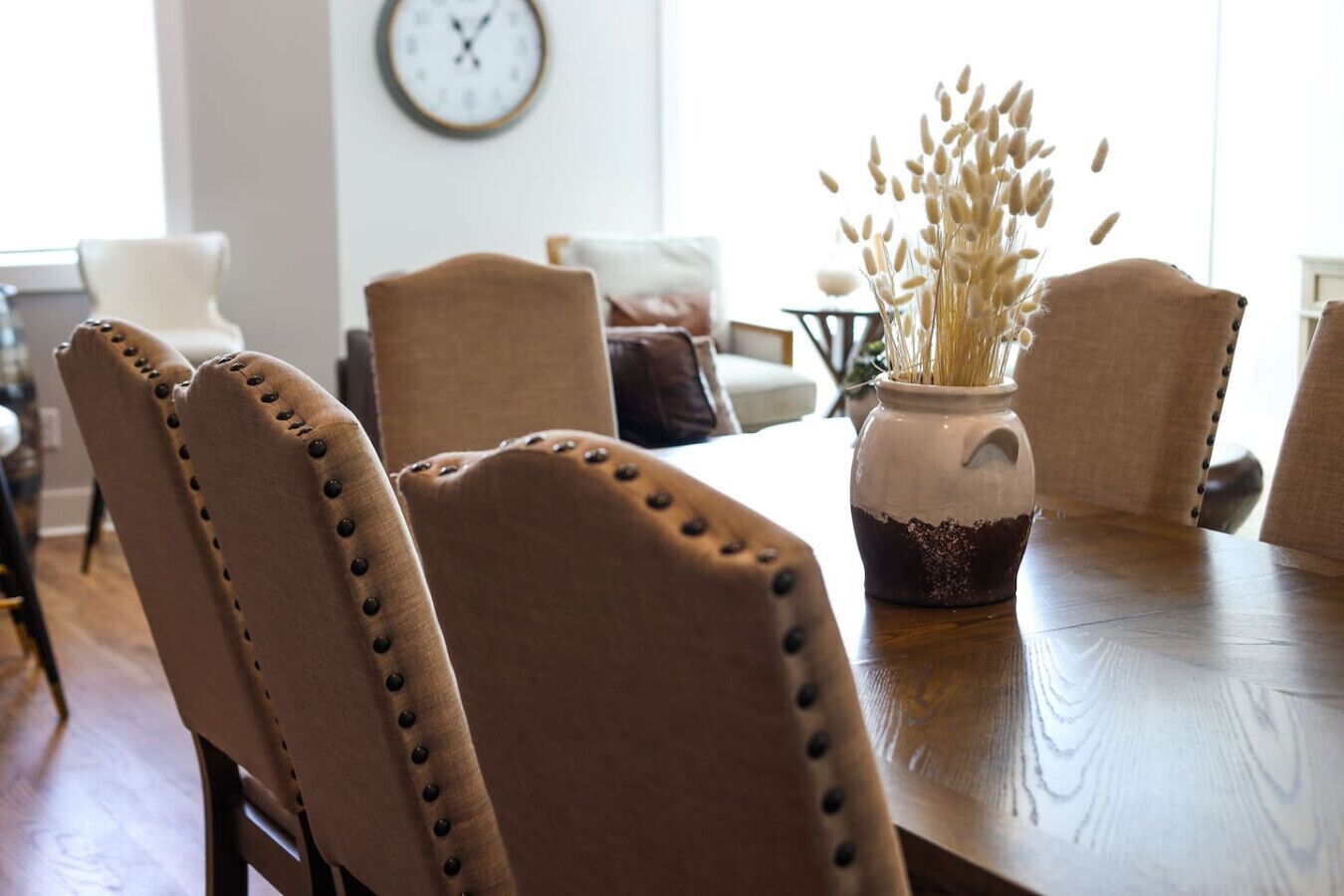 A dining area with a wooden table, four upholstered chairs with button details, and a vase with dried plants.