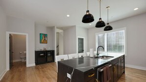 A modern kitchen with a large island, white chairs, and pendant lights. - Two Townhomes | Rooftop Lounges | Skyline Views (Nashville)