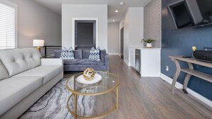 Un salon moderne avec un canapé gris, une table basse ronde en verre et un divan gris.