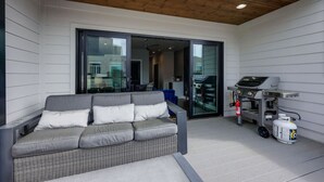Un espace de vie extérieur moderne, doté d’un canapé gris, d’un coin barbecue et d’une porte-fenêtre coulissante donnant sur un espace intérieur.