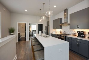 A modern kitchen with a central island, stainless steel appliances, and pendant lighting. - Two Townhomes- West End Rooftop Patios (Nashville)