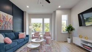 A modern living room with a blue sofa, pink chairs, a coffee table, and a TV on the wall. - Hey, Nashville! & Dolly & Denim - Dual Townhomes (Nashville)