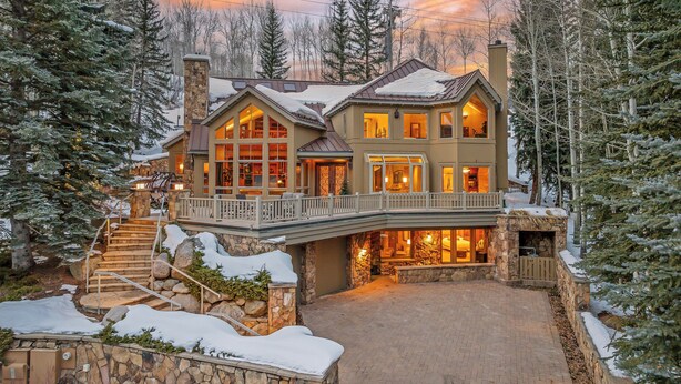 A large, multi-story lodge with a stone facade, large windows, and a balcony overlooking a snowy landscape. - Large Ski-in/out Retreat + Lap Pool | Founders Lodge (Beaver Creek)