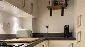 A modern kitchen with white cabinets, a built-in oven, a toaster, and a coffee maker. - House-sleeps3-parking-garden-petfriendly (Nottingham)