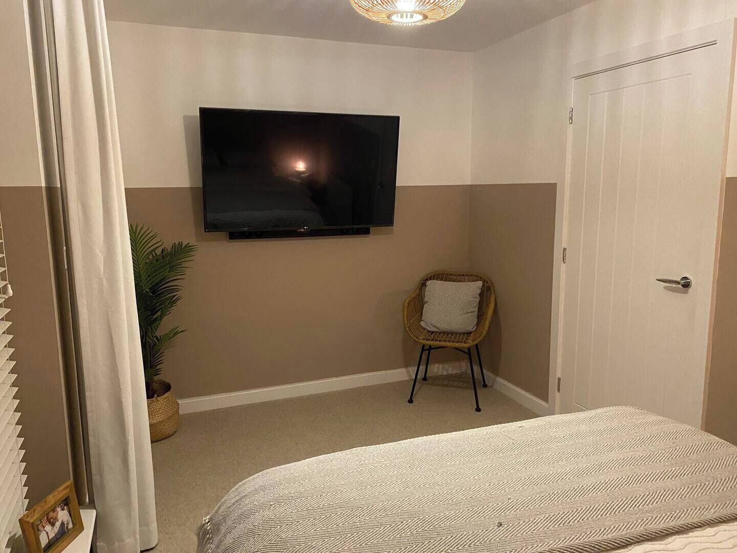 A bedroom with a bed, a television mounted on the wall, a chair, and a door.