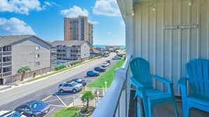 A balcony with blue chairs, a view of a street with parked cars, and a tall building in the background.