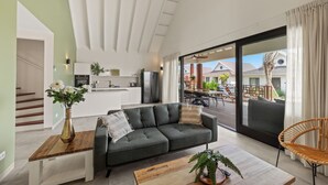 A modern living room with a sectional sofa, a wooden coffee table, and a dining area with a table and chairs. A large sliding glass door leads to an outdoor patio.