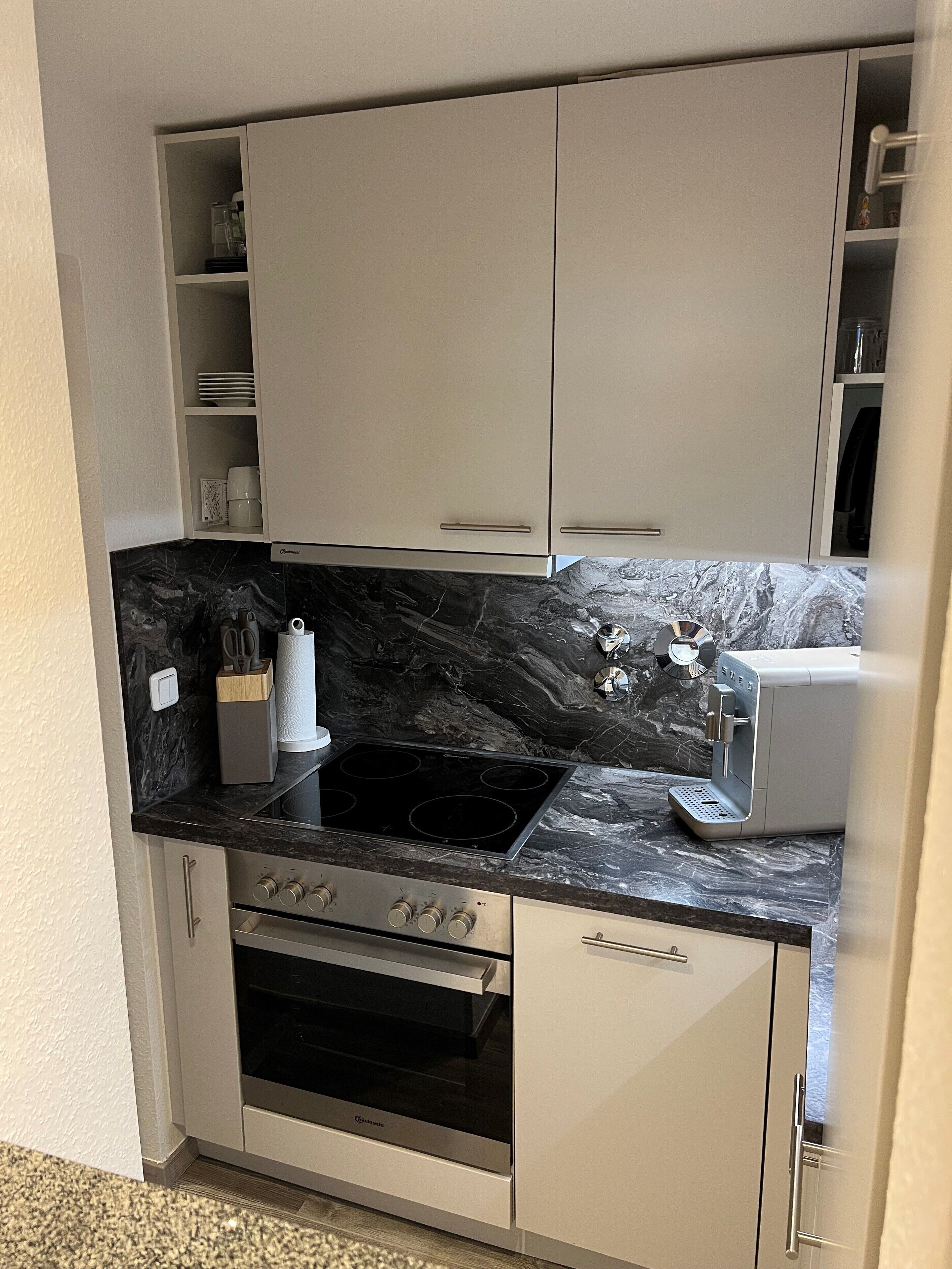 A compact kitchen with white cabinets, a black marble countertop, a built-in oven, and a coffee maker.