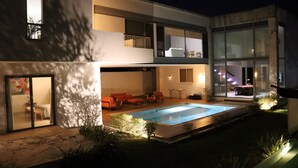 Ett modernt hus i två våningar med en swimmingpool, utomhusmöbler och en balkong.