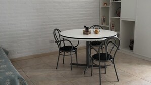 Un comedor con una mesa redonda y cuatro sillas, una pared de ladrillo blanco y una estantería blanca con objetos decorativos.