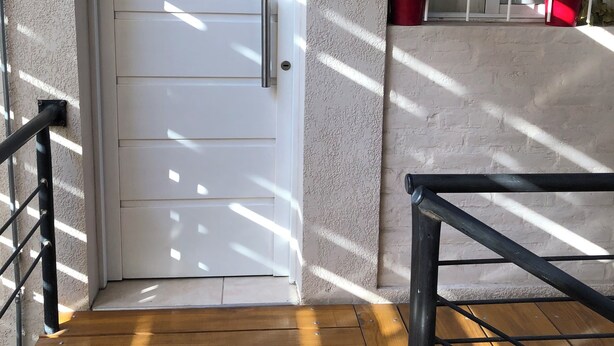Una puerta blanca con manija, una escalera de madera con barandas de metal y una ventana con vistas al exterior.