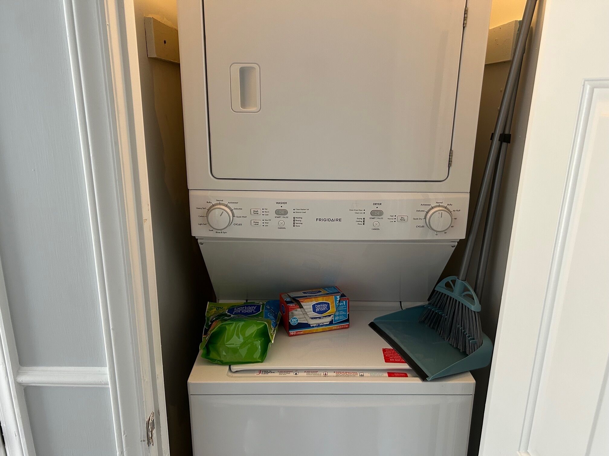 En vaskemaskine og tørretumbler i ét, med et kontrolpanel, en grøn pose vaskemiddel og en kasse vaskemiddel ovenpå.