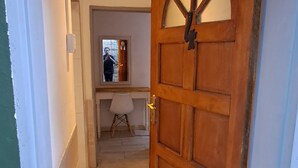 A hallway leading to a room with a wooden door, a small table, and a chair.