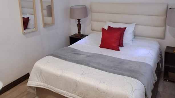 A bedroom with a bed, a nightstand, a lamp, and a cowhide rug.