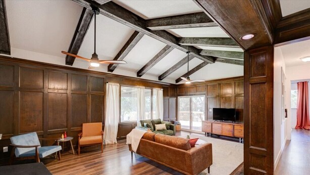 A spacious living room with wooden floors, a brown sofa, a television, and a large window.