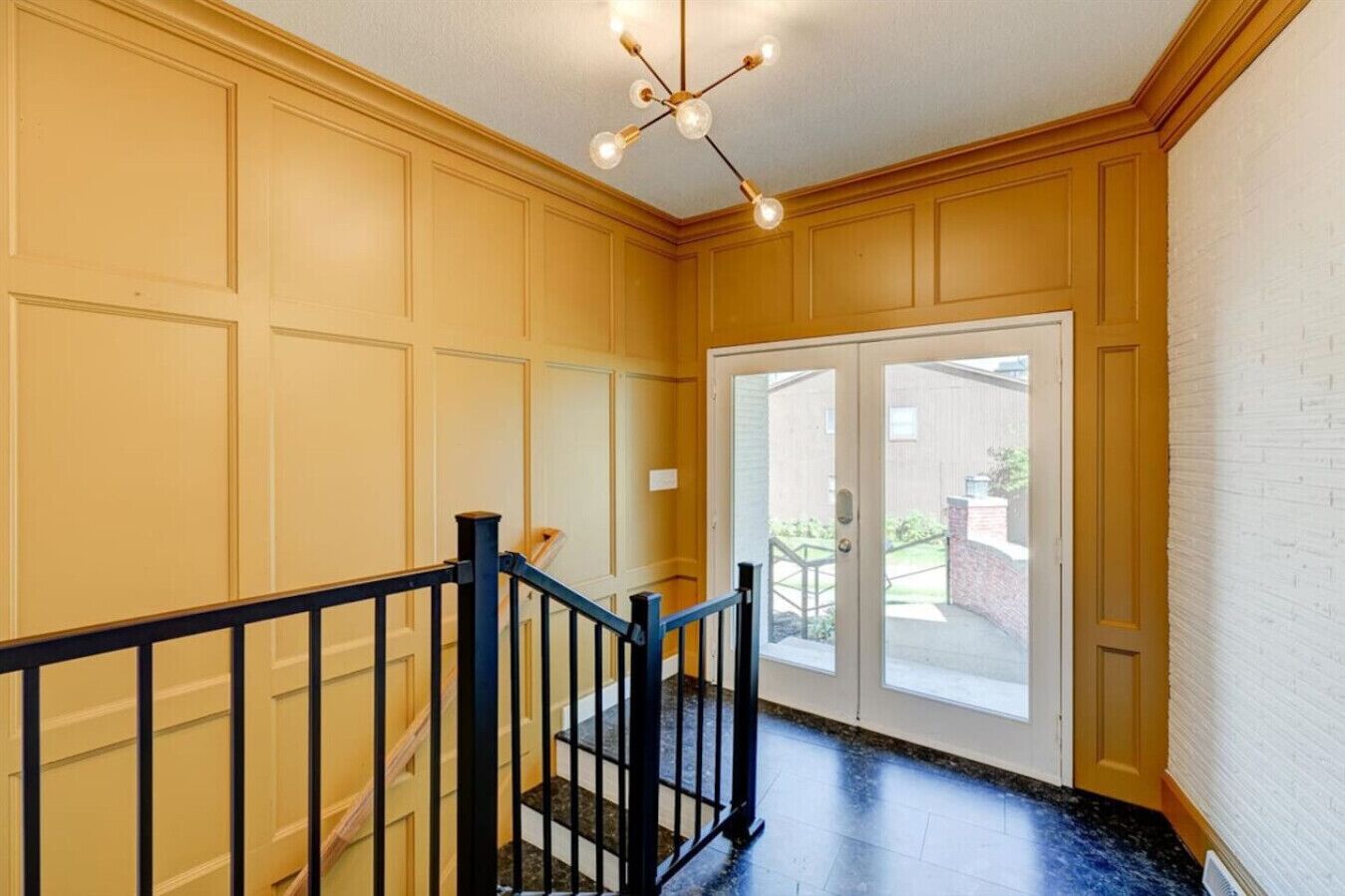A hallway with a black railing, a door with glass panels, and a ceiling light fixture.