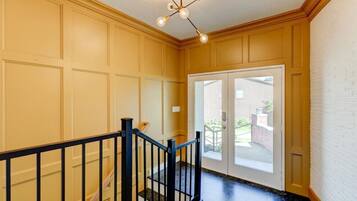 A hallway with a black railing, a door with glass panels, and a ceiling light fixture.