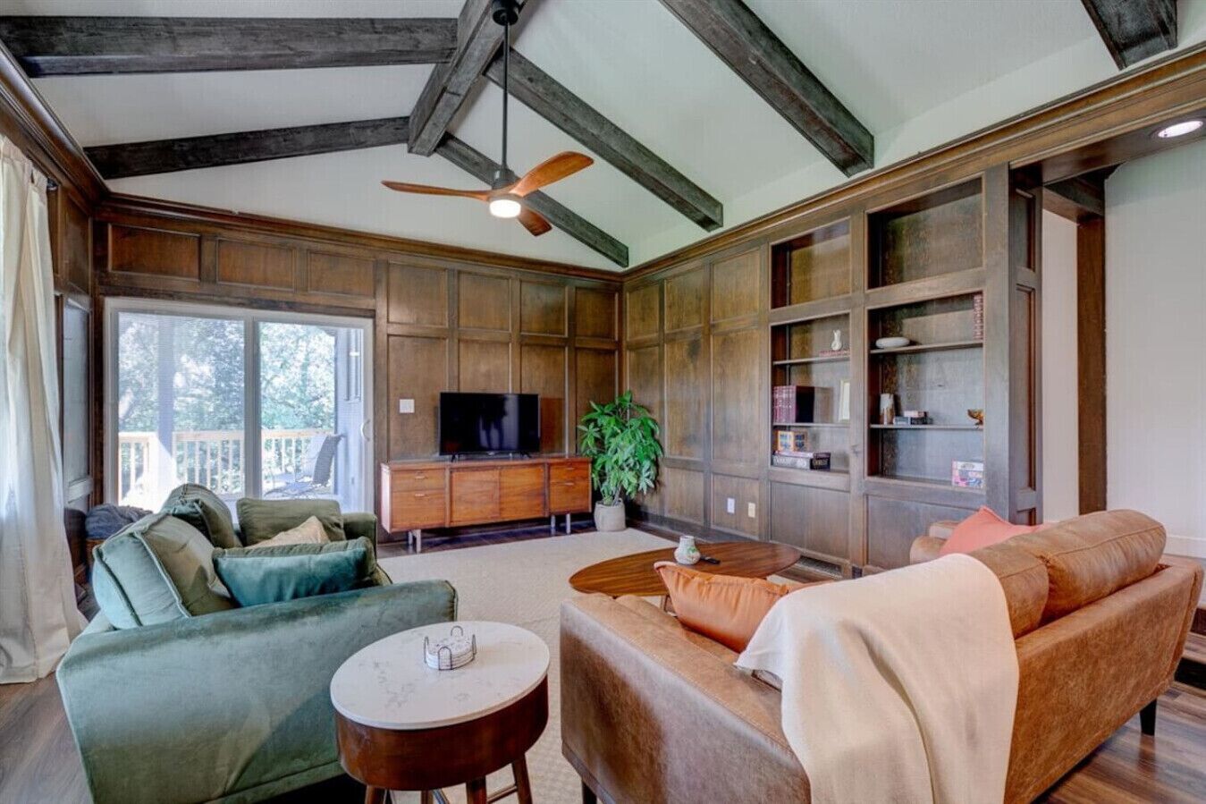 A spacious living room with a large TV, wooden paneling, and a ceiling fan.