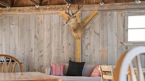 A rustic wooden interior with a deer head mounted on the wall, a wooden bench with cushions, and a table with chairs.