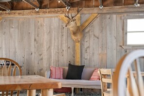A rustic wooden interior with a deer head mounted on the wall, a wooden bench with cushions, and a table with chairs.