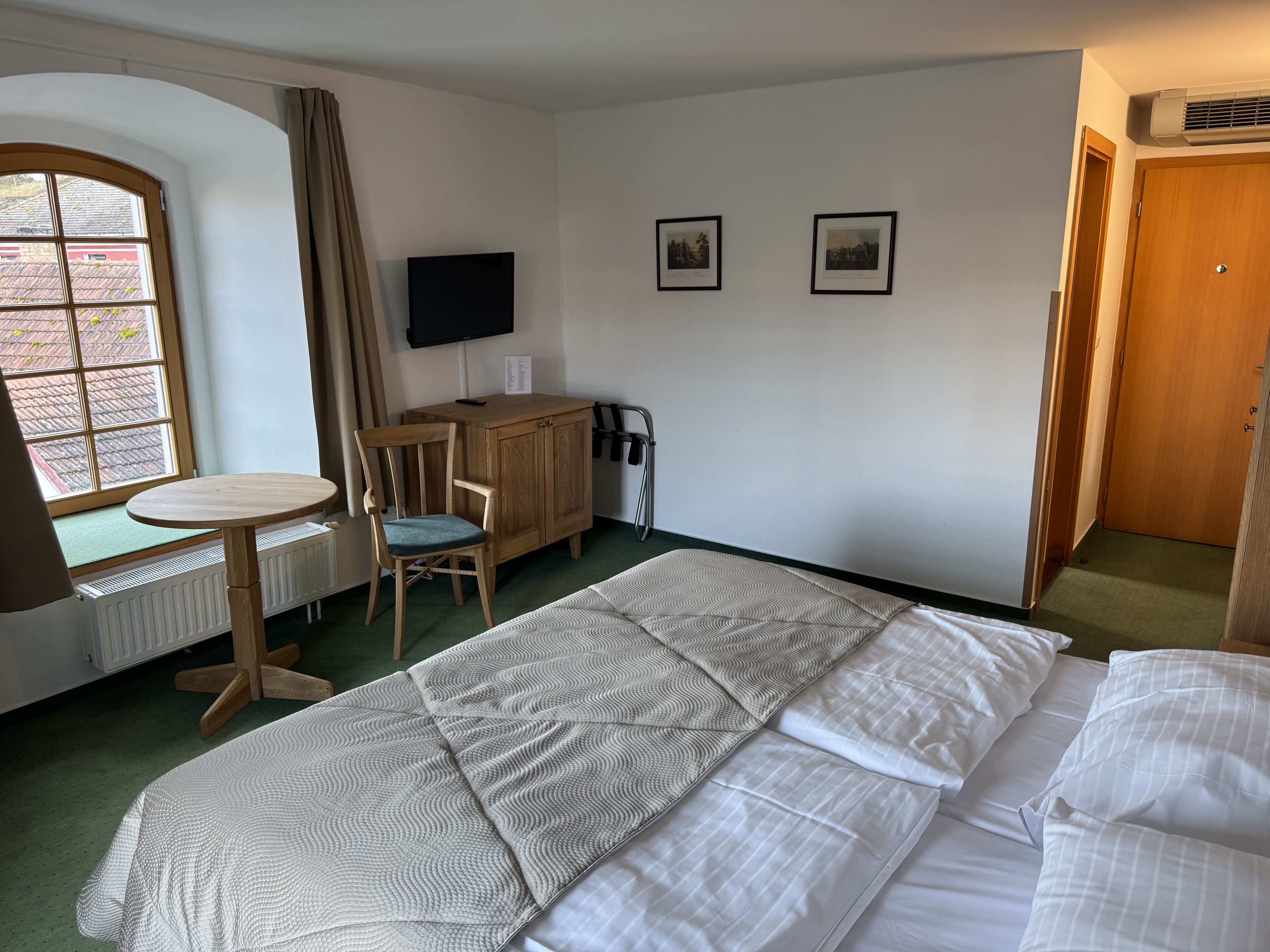 Una habitación de hotel con una cama, un escritorio con una silla, un televisor y dos cuadros en la pared.