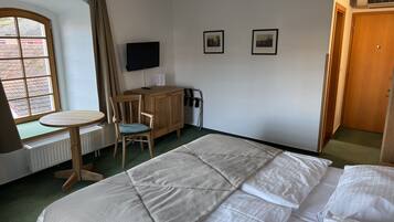 Una habitación de hotel con una cama, un escritorio con una silla, un televisor y dos cuadros en la pared.