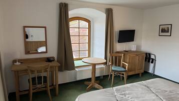 Ett hotellrum med en säng, ett skrivbord med en stol, ett litet bord, en tv och ett fönster med gardiner.