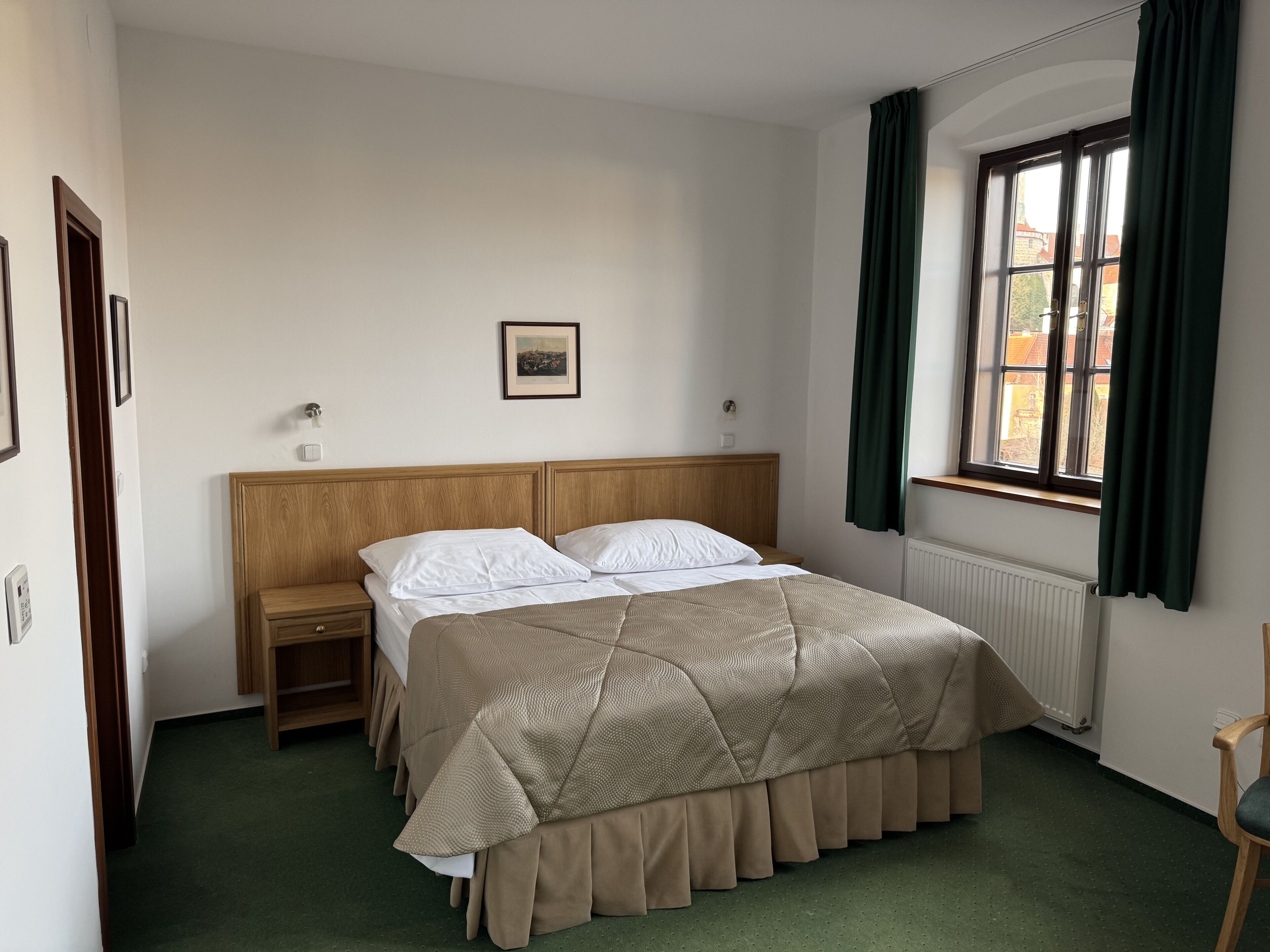 A hotel room with a bed, a nightstand, a framed picture on the wall, and a window with curtains.