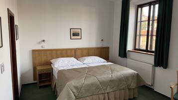 A hotel room with a bed, a nightstand, a framed picture on the wall, and a window with curtains.