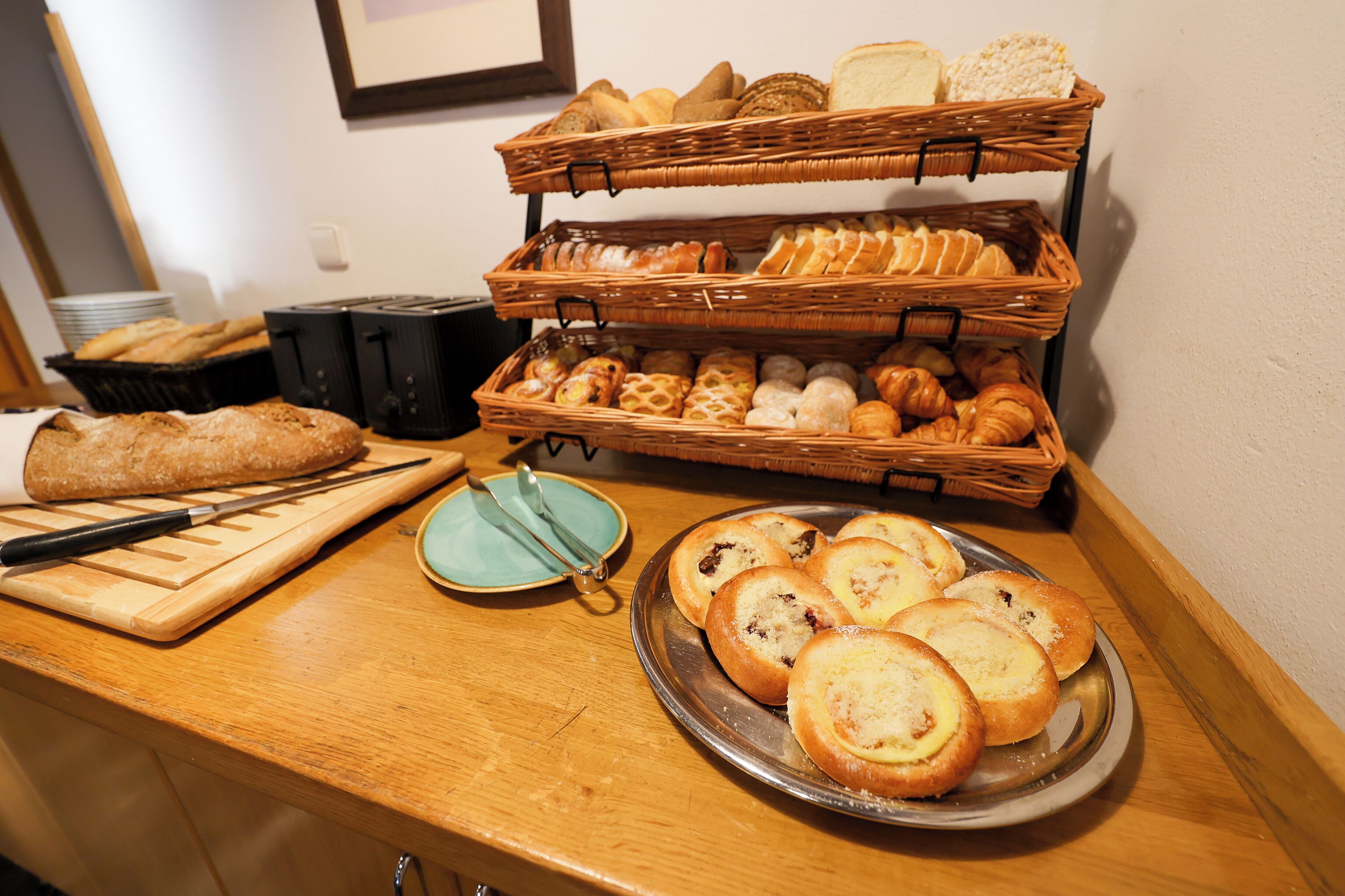 A buffet with various breads and pastries displayed on a wooden counter.