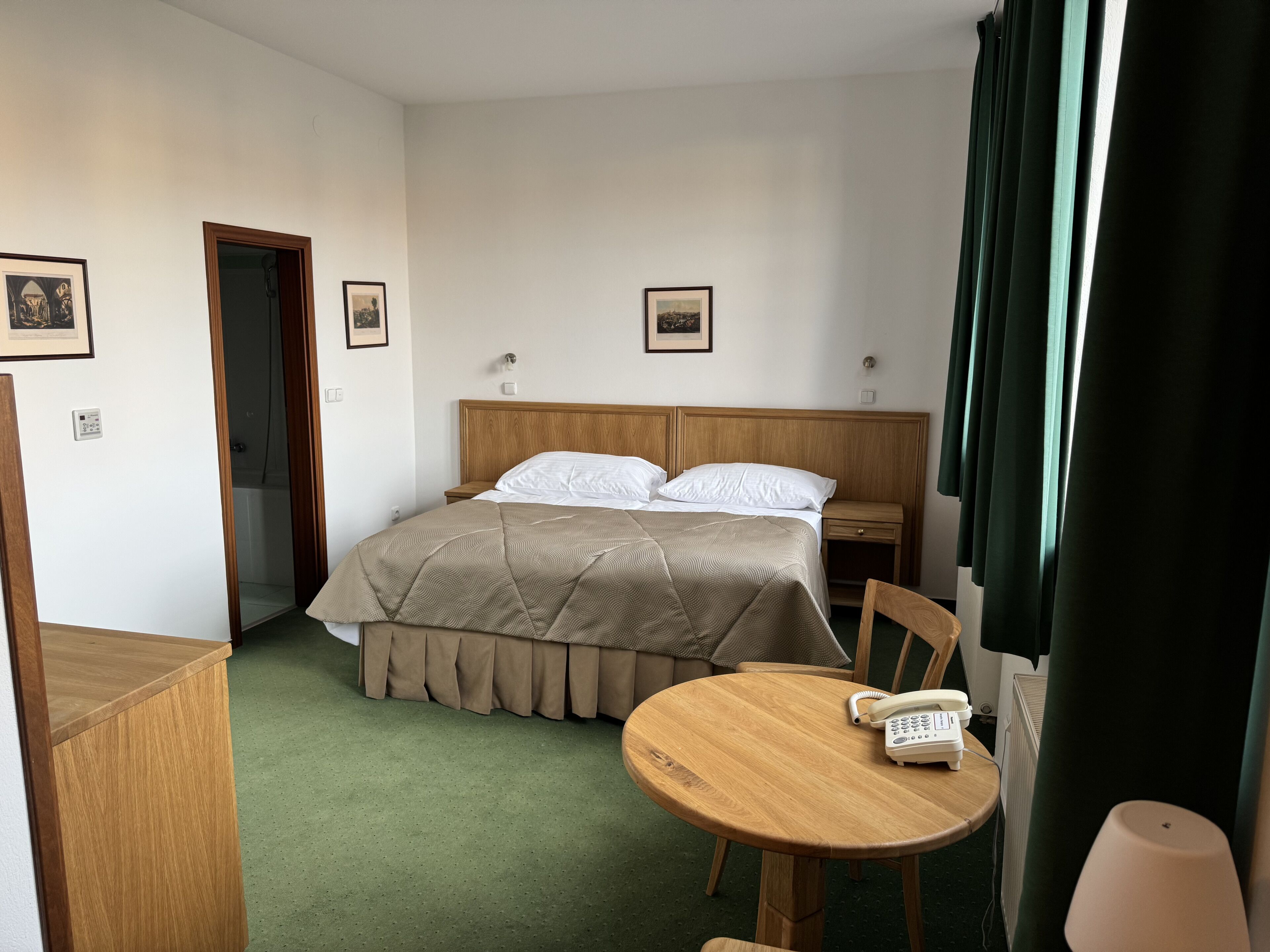Quarto de hotel com cama, mesa de cabeceira, cadeira e pequena mesa com telefone.