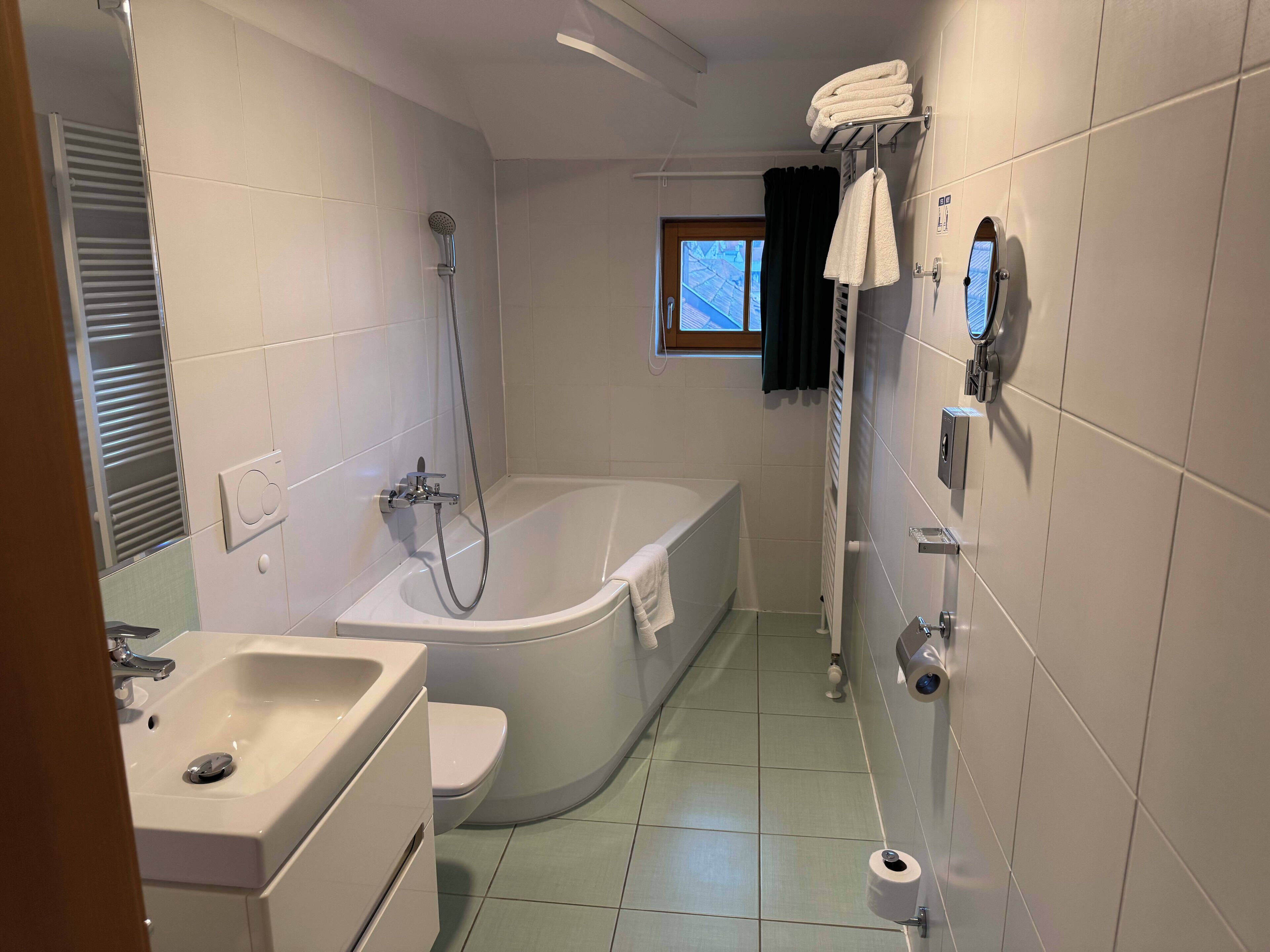 A bathroom with a bathtub, toilet, sink, and a window with curtains.