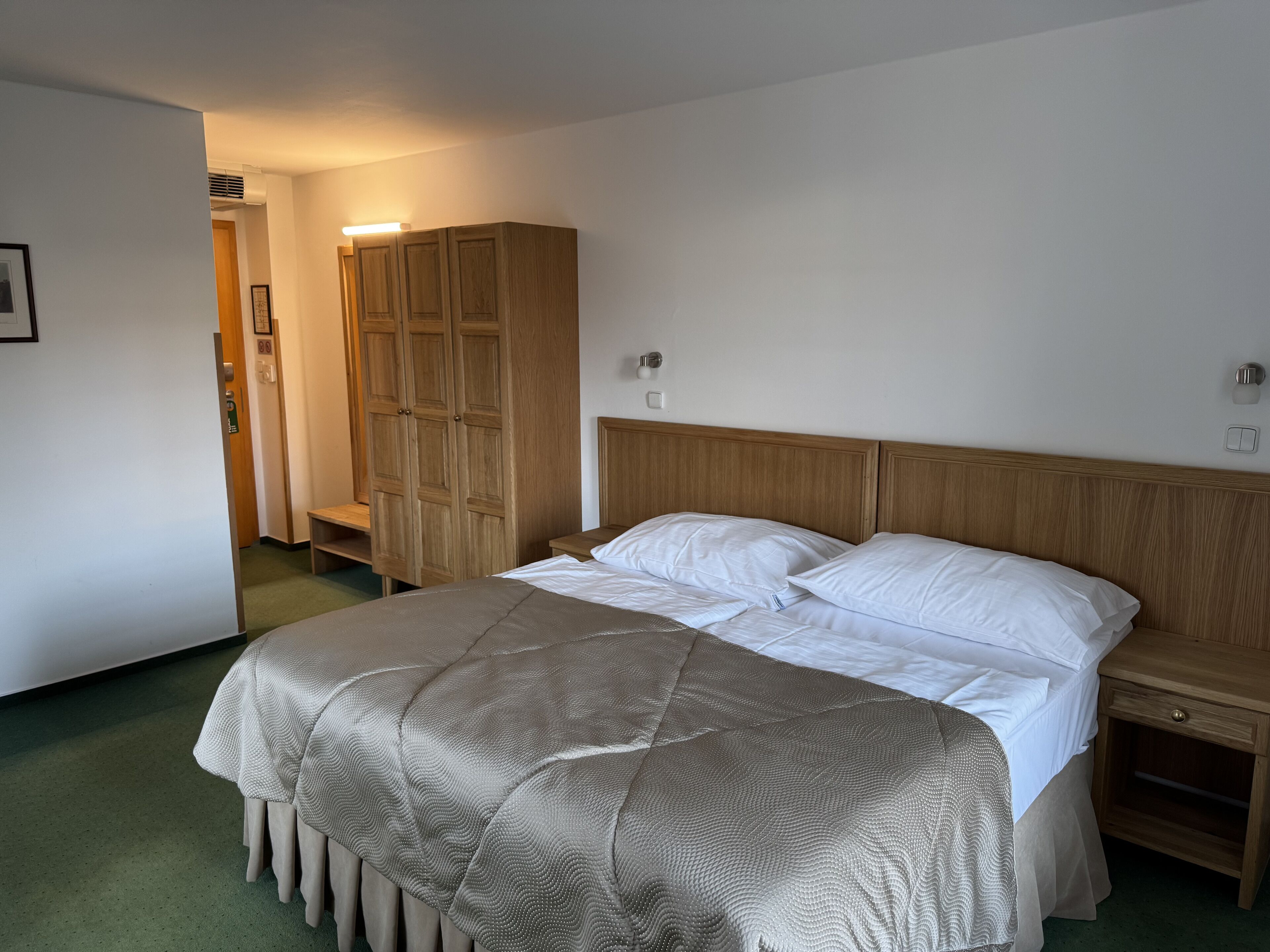 A bedroom with a bed, wooden wardrobe, bedside tables, and a green carpet.