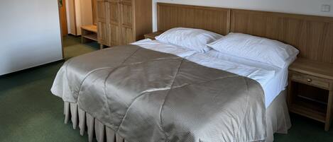 A bedroom with a bed, wooden wardrobe, bedside tables, and a green carpet.