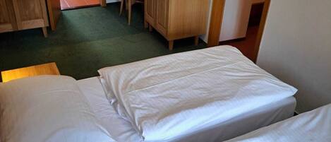 A hotel room with two beds, a wooden desk, a chair, a television, and a bathroom visible through an open door.