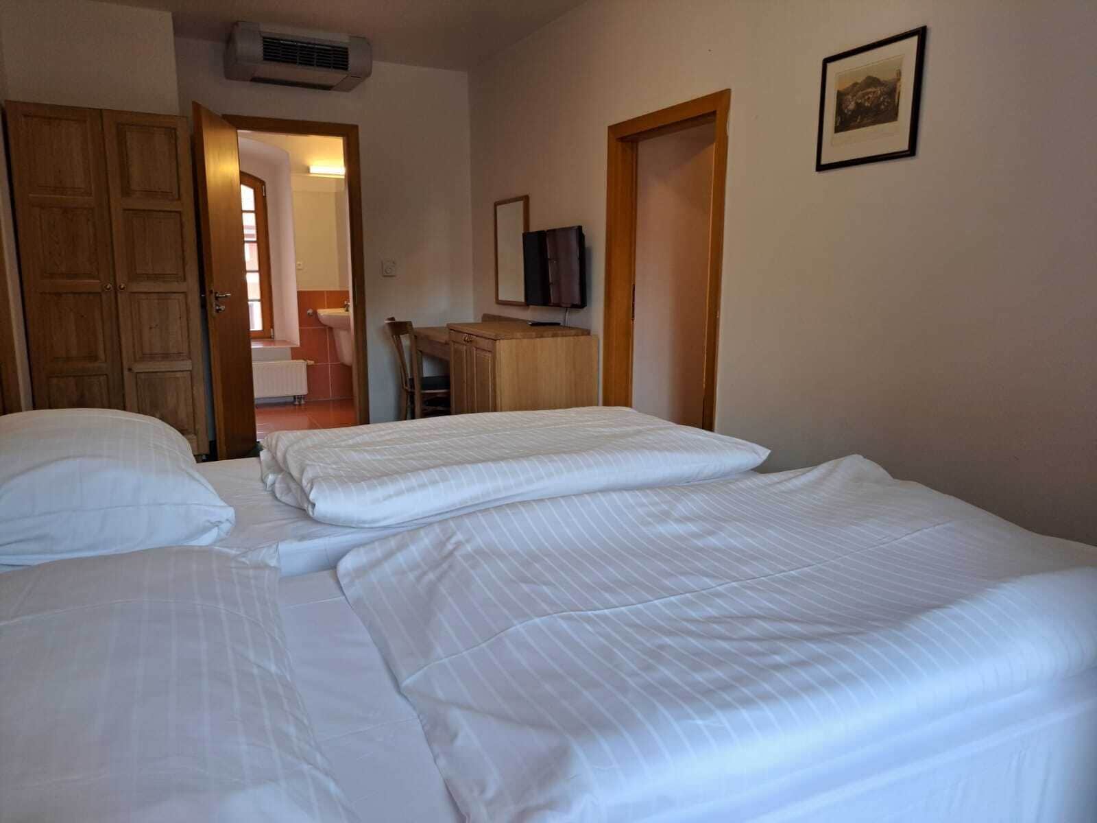 Habitación de hotel con dos camas, un armario de madera, un televisor sobre un mueble de madera y un baño visible a través de una puerta abierta.