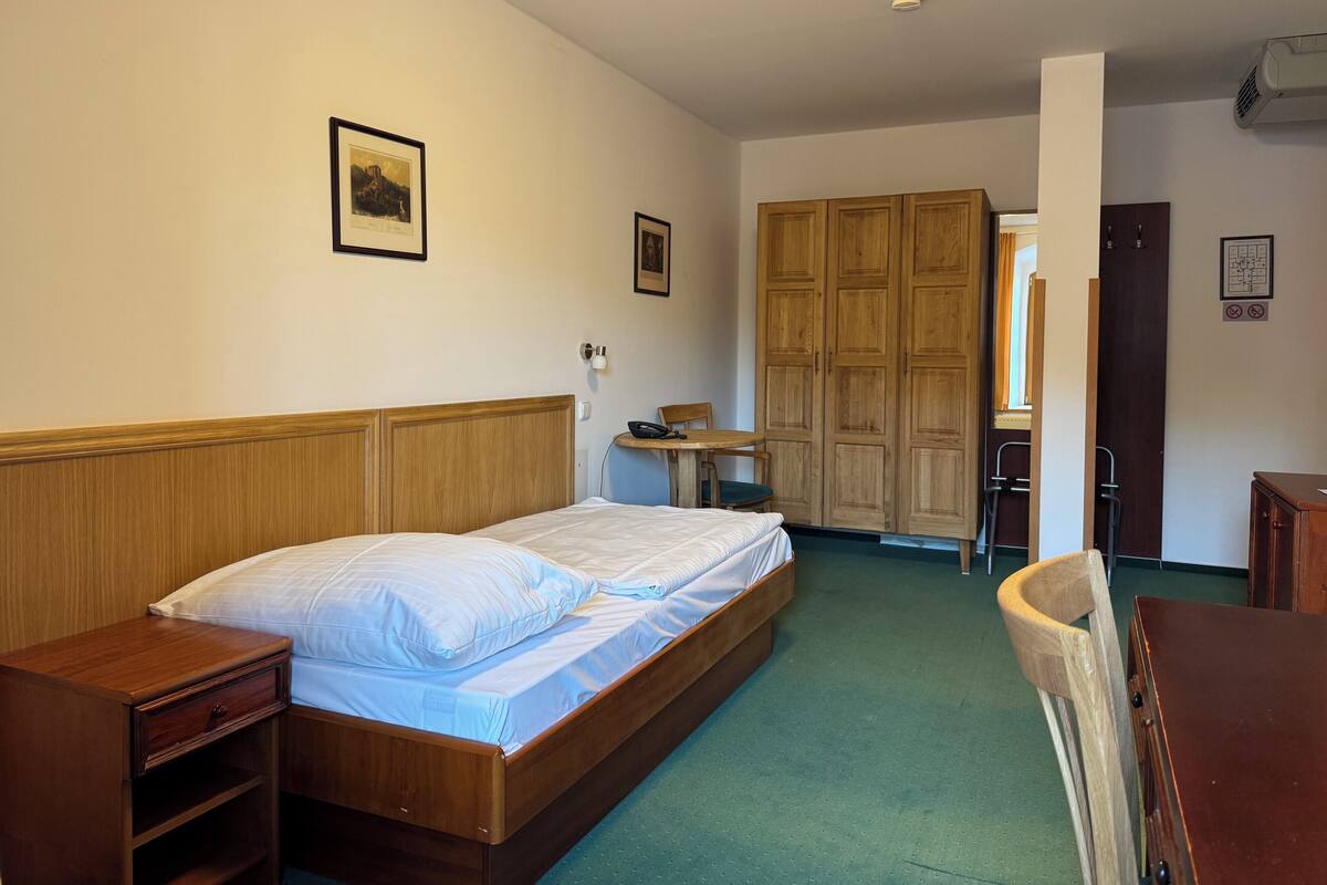 Une chambre d’hôtel avec un lit en bois, un bureau, une chaise et une armoire.